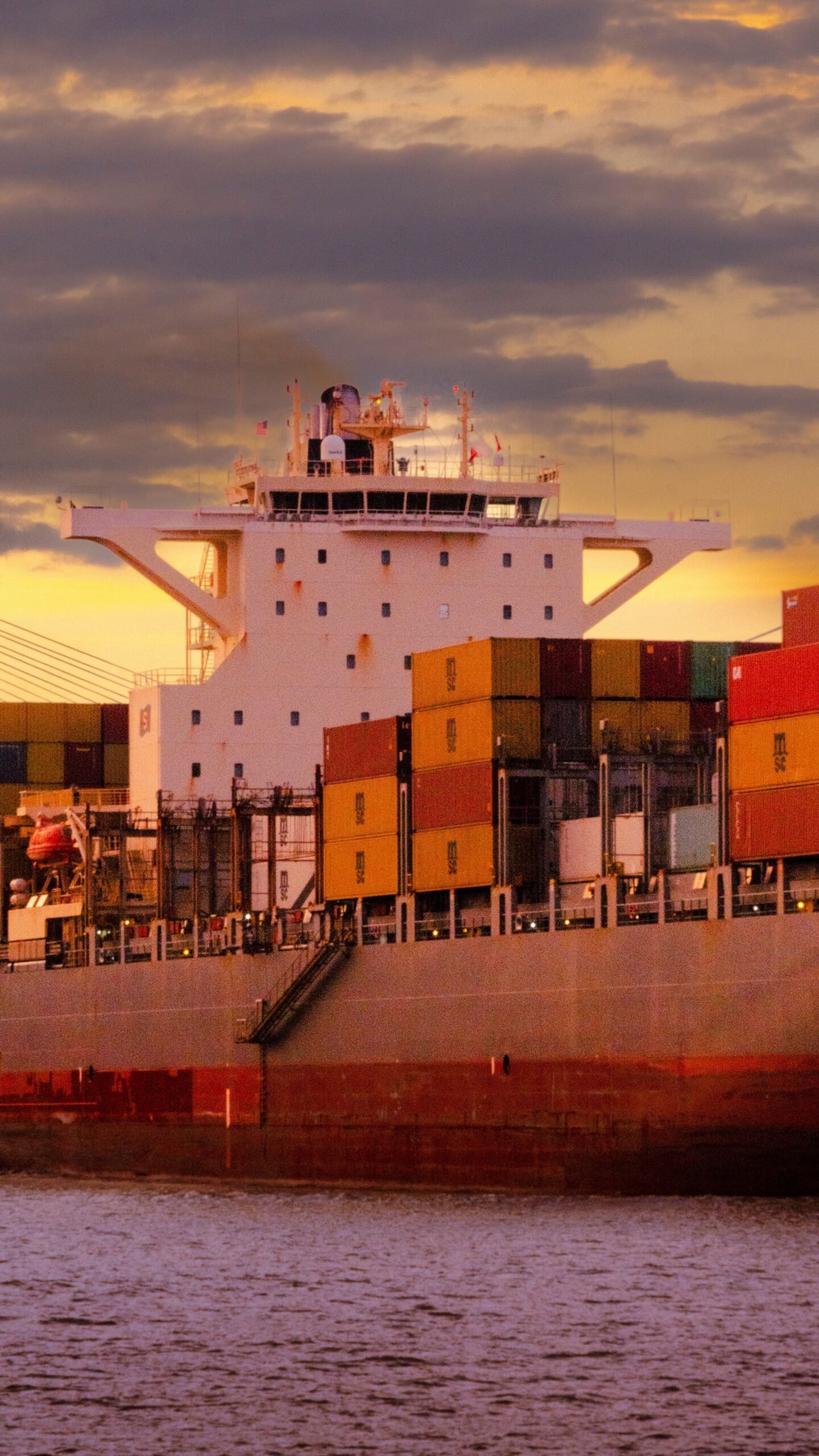 Cargo ship loaded with colorful containers against a vibrant sunset sky.